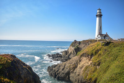 Lighthouse amidst sea and buildings against sky