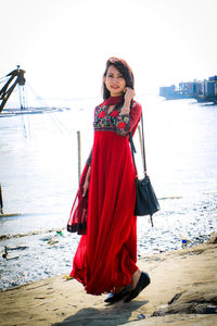 Portrait of young woman standing at beach against sky