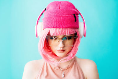 A teenager in headphones with pink hair.  a girl with a short haircut on a blue background.