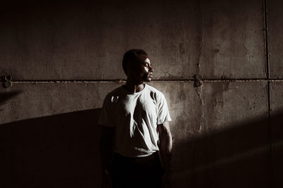 Male athlete standing against gray wall during sunset