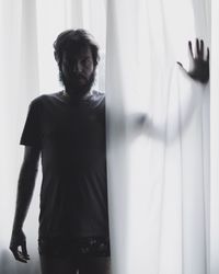 Portrait of mid adult man standing by window at home