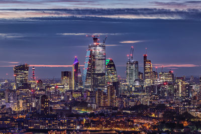 Illuminated buildings in city against cloudy sky