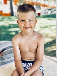 Portrait of shirtless boy sitting by swimming pool