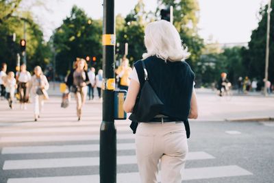 Rear view of senior woman crossing road in city