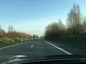 Road amidst trees against sky seen through car windshield