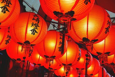 Low angle view of illuminated lanterns hanging against orange sky