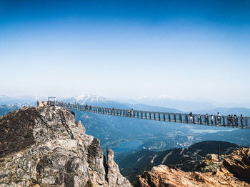 Crowd of people walking on suspension bridge against sky