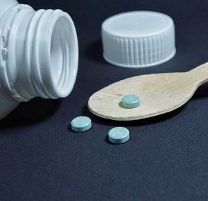 Close-up of medicines with wooden spoon and pill bottle over black background