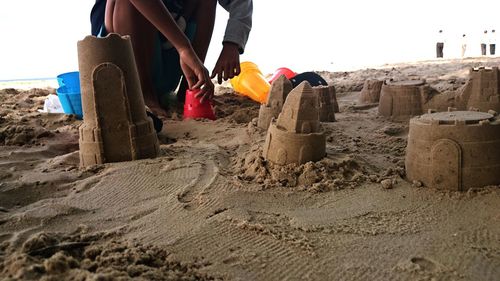 Low section of man relaxing on sand at beach against sky