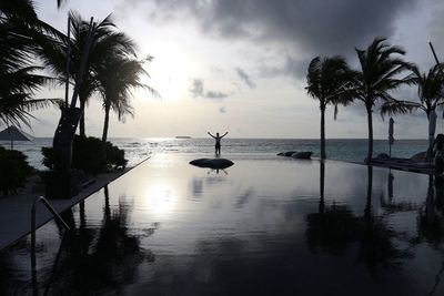 Silhouette palm trees on swimming pool against sky during sunset