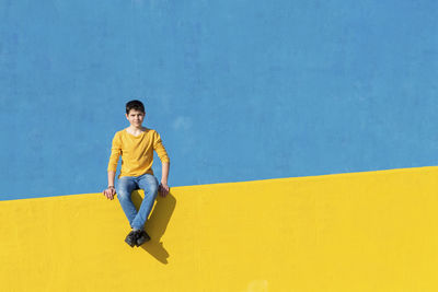 Portrait of boy sitting on yellow railing against blue wall