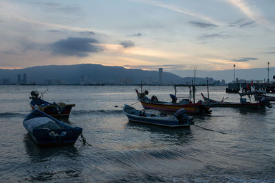 Fishing boats moored in sea against sky during sunset