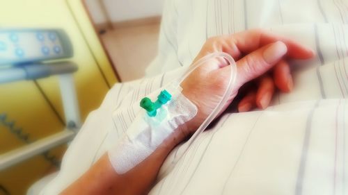 Cropped hand of woman with iv drip on bed in hospital