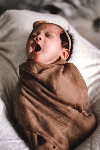 Cute baby girl yawning while lying on bed