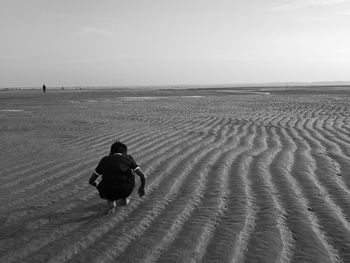 Rear view of man crouching on patterned beach against sky