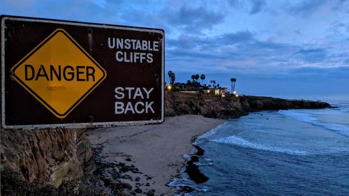 Information sign by sea against sky