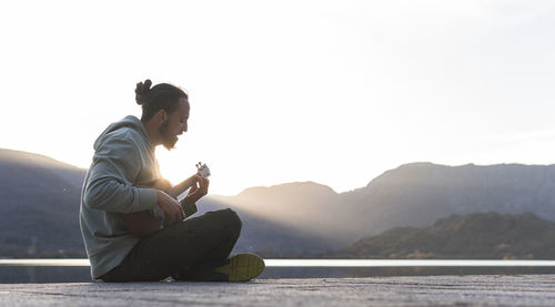 Side view of young man using smart phone against sky