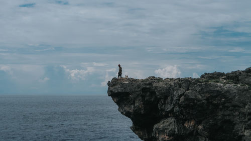 Man standing on rock by sea against sky