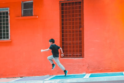 Side view of boy running by red building