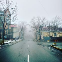 Road by trees in city against clear sky