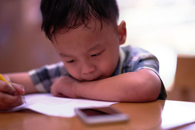 Cute boy writing in book while sitting at table