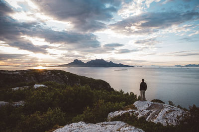 Rear view of man standing on rock against sky