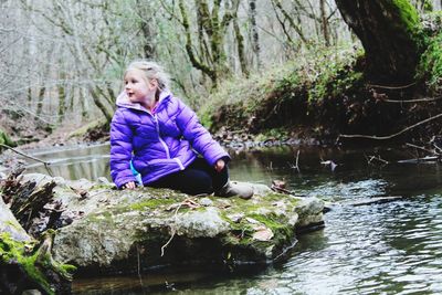 Girl sitting on rock by river in forest