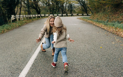 Mom is waiting in her arms for a little daughter running towards her on a walk along a rural road.