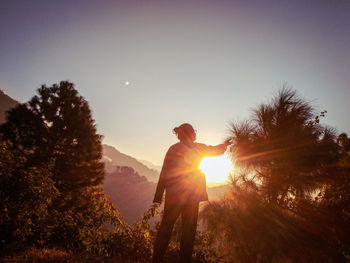 Silhouette man standing by trees against sky during sunset