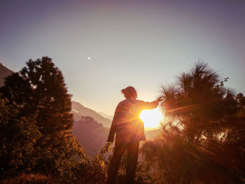 Silhouette woman standing by trees against sky during sunset