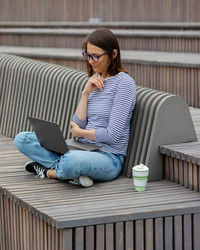Young woman using laptop sitting on wooden seat