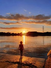 Silhouette woman standing at beach against sky during sunset