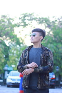 Young man wearing sunglasses standing against car