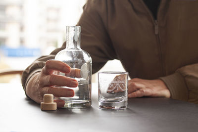 Midsection of man holding glass bottle on table