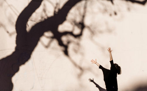 Side view of woman gesturing towards tree shadow on wall