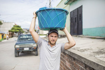 Caucasian man carries basket on top of his head.