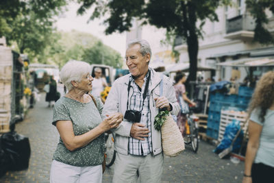 Happy senior couple talking while walking arm in arm at street market
