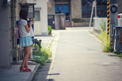 Young woman using phone while standing on footpath