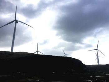 Low angle view of wind turbines on field against sky