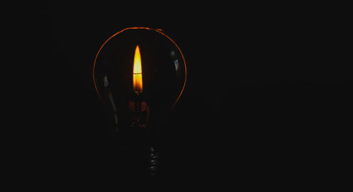 Close-up of illuminated candle behind light bulb against black background