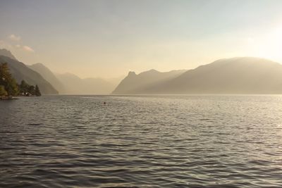 Scenic view of lake by mountains against sky during foggy weather