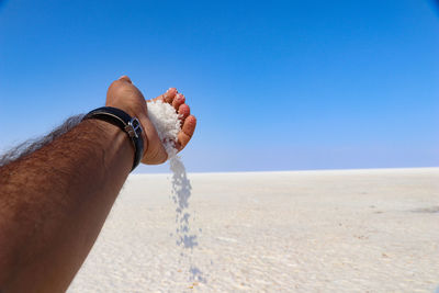 Low section of man on sand at beach against clear blue sky