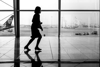 Silhouette woman standing by glass window at airport against sky