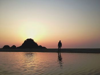 Silhouette man standing by sea against sky during sunset
