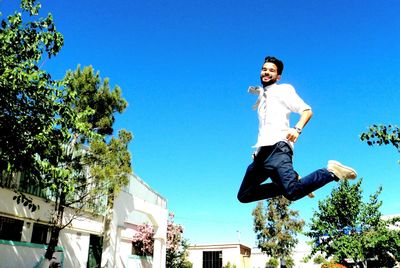 Low angle view of man jumping against blue sky