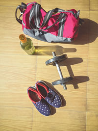 High angle view of dumbbell with shoes and bottle by bag on hardwood floor