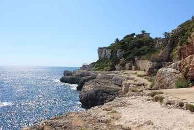 Rocks by sea against clear sky