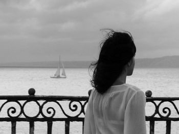 Rear view of woman standing by railing against cloudy sky