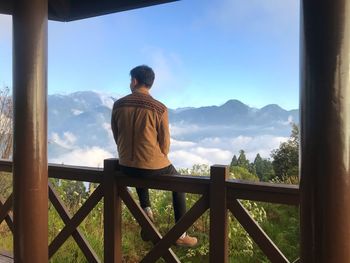 Rear view of man sitting on railing against mountains