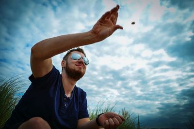 Low angle view of man throwing stone against cloudy sky